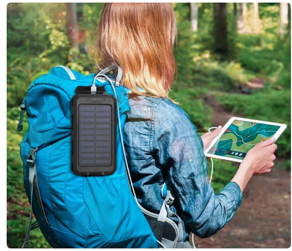 a woman holding a tablet and is charging it with a solar phone charger attached to her bag pack